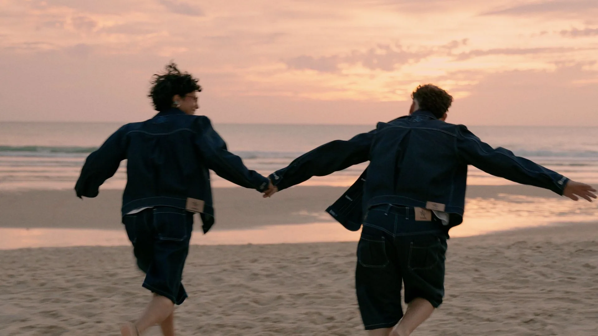 Deux silhouettes courent main dans la main sur la plage