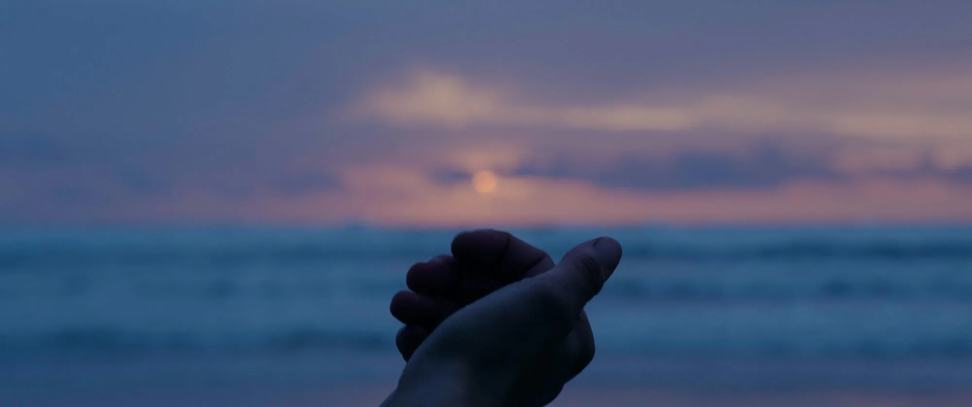 Une main tendue vers le soleil couchant sur la mer