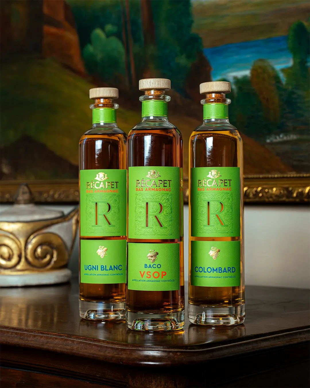 Trois bouteilles d’armagnac Récapet devant un tableau